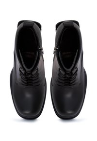 Botas de cuero negras hasta el tobillo con puntas redondas, cordones en la parte delantera y un pequeño zipper a cada lado. Textura suave con un interior acolchado.