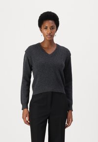 Maglione grigio scuro a collo a V con maniche lunghe, texture morbida e orlo a coste, abbinato a pantaloni neri a gamba dritta. Nessun motivo visibile o accessori metallici.