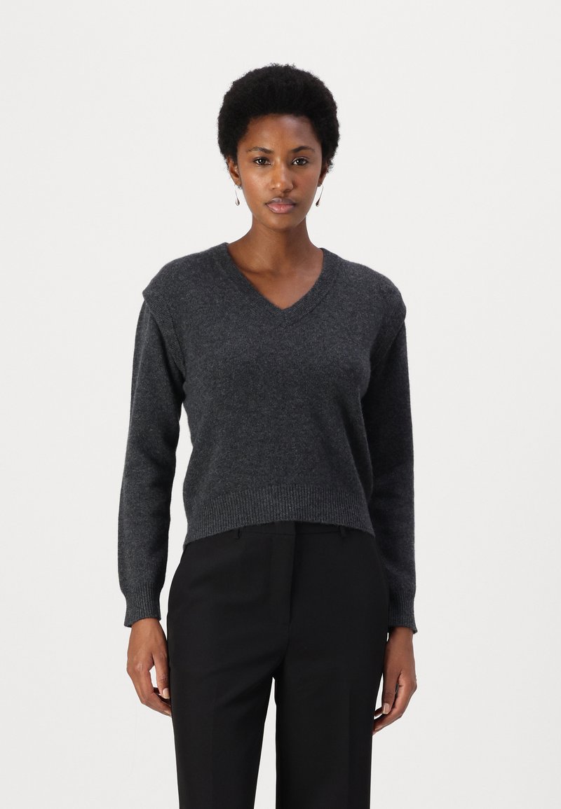 Maglione grigio scuro a collo a V con maniche lunghe, texture morbida e orlo a coste, abbinato a pantaloni neri a gamba dritta. Nessun motivo visibile o accessori metallici.