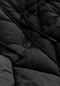 Must kohverjope tikandmustriga. Sellel on must nupp ja paelapidemed. Sile tekstuur ja kerge kangas.