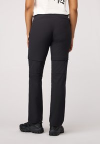Pantalons de randonnée légers noirs à coupe droite, dotés de poches zippées et de coutures renforcées, associés à des chaussures de randonnée noires.
