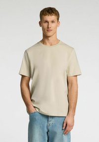 Beige, short-sleeve t-shirt with a round neck and plain design, made of soft fabric. Worn with light blue denim jeans.