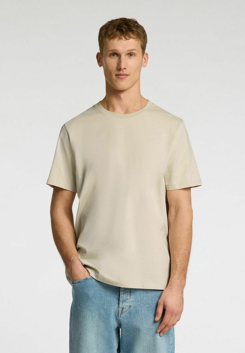 Beige, short-sleeve t-shirt with a round neck and plain design, made of soft fabric. Worn with light blue denim jeans.