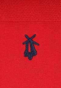 Czerwona tkanina o dzianym wzorze z ciemnoniebieskim wyszywanym logo, umieszczonym w dolnym lewym rogu.