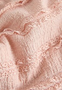 Helles rosa Stoff mit strukturierter Oberfläche, mit gewellten Kanten und zarter Spitze mit durchbrochenen Mustern. Weiches und geschichtetes Design.