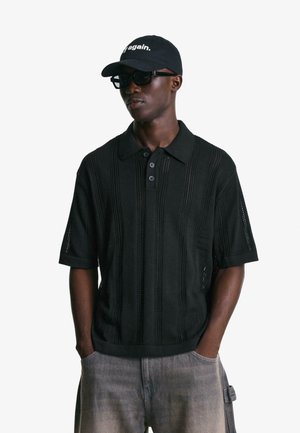 Black short-sleeve polo shirt with textured pattern and three buttons. Worn with light gray pants. Accessories include black cap and sunglasses.