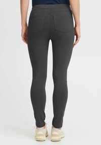 Sivi skinny jeans z gladko teksturo, s srednje visokim pasom, dvema zadnjima žepoma in prilegajočimi nogami, v kombinaciji z svetlimi supergami.