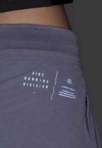 Gros plan de la taille portant un short gris Nike Running Division avec une ceinture en mesh et une poche latérale zippée.