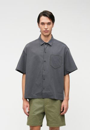 Chemise à manches courtes en tissu gris foncé avec une poche poitrine, coupe décontractée et texture lisse, associée à un short vert clair.