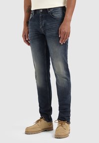 Donkerblauwe denim jeans met een slim fit, met vervaging langs de dijen en vijf zakken, gecombineerd met tan suède schoenen.