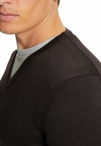 Maglione scuro marrone a V in tessuto a maglia struttura, indossato sopra una camicia grigia chiara. Presenta un colletto a costine e dettagli sulle spalle.