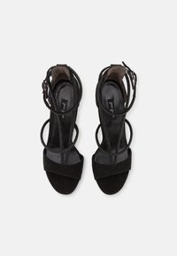 Sandalias de tacón alto de ante negro con un diseño de tiras, que cuentan con una banda frontal ancha y tiras finas en el tobillo. Forro interior suave.