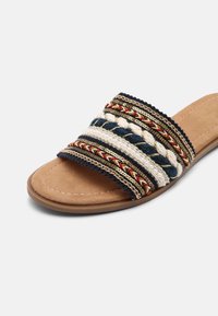 Sandale slide avec semelle rembourrée couleur fauve et large bride ornée de motifs tressés et perlés en bleu marine, blanc, rouge et touches dorées.