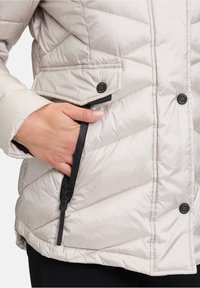 Lettet puffer-jakke i lys beige med diagonalt quiltet design, sort lynlåslomme og trykknaplukninger. Lavet af glat, vandafvisende materiale.