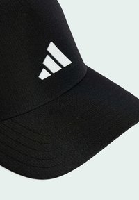 Casquette noire au design épuré, avec un logo Adidas blanc. Le tissu semble lisse avec des coutures visibles et une visière courbée.