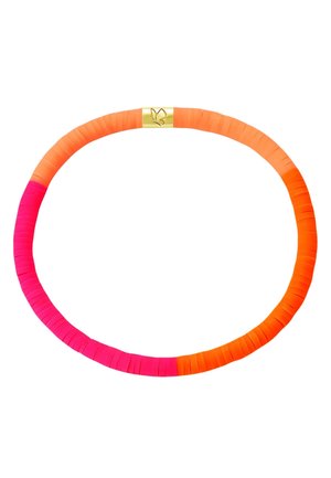 Poignet avec un bracelet fin en perles dans des nuances de rose et de corail sur une personne portant une chemise blanche, main près du visage.