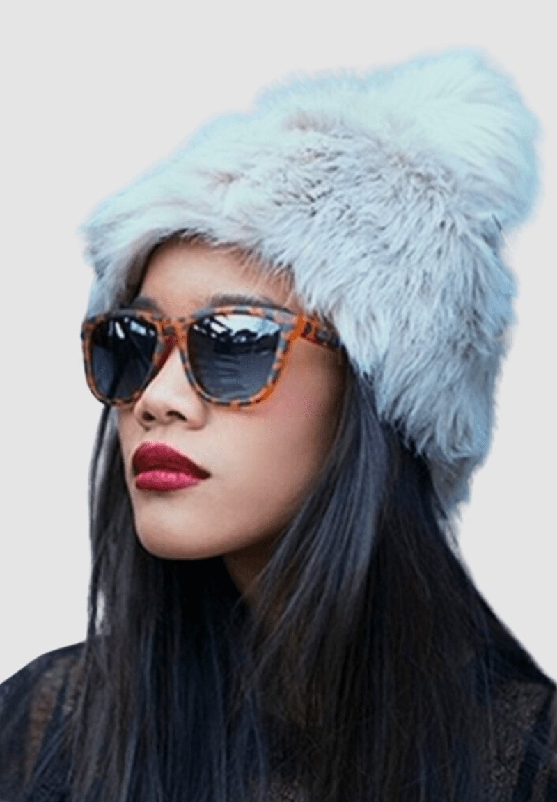 Gorro de piel sintética en gris claro con un pompón en la parte superior. Gafas de sol de carey con lentes oscuros y una parte superior negra texturizada por debajo.