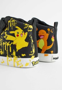 Zwarte sneakers met gele accenten, met ontwerpen van Pikachu en Charmander. Geweven stof met een witte zool en "Pokémon"-branding.