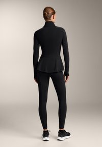 Black athletic top with a high collar and peplum design, paired with black leggings and black athletic shoes. Smooth, stretchy fabric.