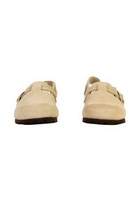 Beige suède schoenen met een open achterkant, voorzien van twee bandaccenten en een gebogen teenontwerp. Rubber zool met een profiel met een lage hoogte.