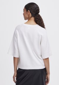 Witte gebreide trui met korte mouwen, ribgebreide zoom en naaddetails achter. Zachte textuur, ontspannen pasvorm en lichte uitstraling.