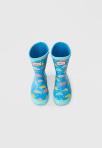 Bottes de pluie en caoutchouc bleu avec un motif de nuages dans des couleurs pastel. Accentuées d'une bordure bleu clair et d'une étiquette de logo en haut.
