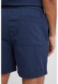 Granatowe, teksturowane szorty z elastycznym pasem, wyposażone w tylnią naszywaną kieszeń i obszyty mankiet dla dopasowanego wyglądu.