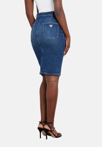 Džinsinė pieštuko sijonas, iki vidurio šlaunų, tamsiai mėlynos spalvos, struktūruotas kirpimas, su mažuoju logotipo užkliju ir siuvimo detalėmis ant galinio kišenės.