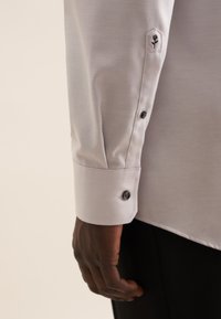 Witte button-up shirt met een gladde textuur, voorzien van een bloemenborduursel op de manchetten en donkere knopen langs de mouw.