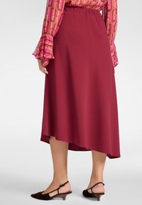 Falda midi color vino con dobladillo asimétrico, hecha de un tejido suave. Combinada con zapatos slingback marrones con tacón de madera.