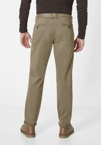 Khaki chinos with a smooth texture, rolled cuffs, and two back pockets. Paired with brown shoes and a fitted dark sweater.