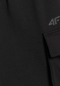 Tissu noir avec une poche à rabat détaillée par des coutures et un petit logo "4F" gris clair près du bord supérieur de la poche.
