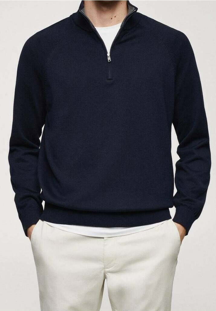Pull-over bleu marine à col zippé 1/4, fabriqué en tissu tricoté doux. Il présente des manches longues et un ourlet côtelé. Associé à un pantalon blanc.