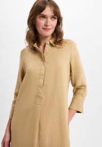 Licht beige shirtjurk van ademende stof, met een kraag, knopen, driekwart mouwen en zijzakken.