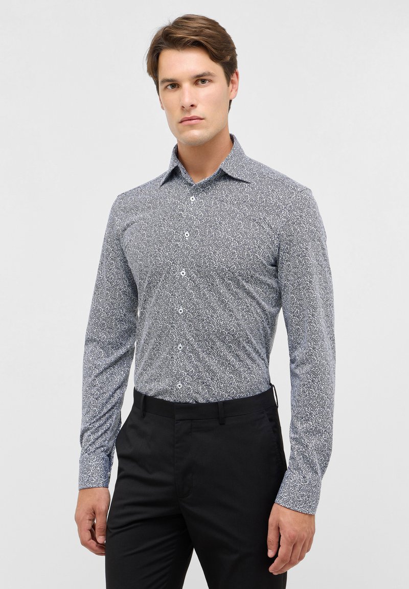 Langarmshirt in een blauw-wit abstract patroon, met een aansluitend ontwerp, standaard kraag en knoopsluiting aan de voorkant. Gecombineerd met zwarte broek.