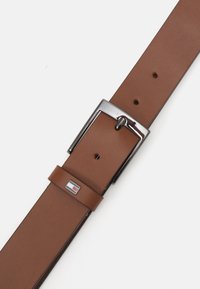 Cintura in pelle marrone con una fibbia argentata lucida; presenta un design rettangolare e più fori per la regolazione delle misure. Logo del brand incluso.