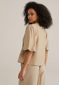 Beige, kurzes Oberteil aus strukturiertem Stoff mit Puffärmeln und lockerer Passform, kombiniert mit passenden beige Hosen.