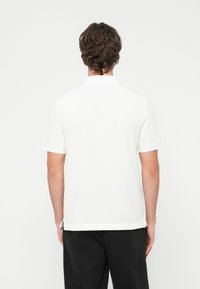 Λευκό �πόλο μπλουζάκι με κοντά μανίκια, με κλασικό γιακά και ανοίγματα στα πλαινά στο τελείωμα. Κατασκευασμένο από μαλακό ύφασμα, με λεία υφή.