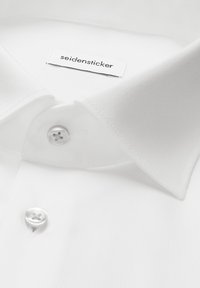 Chemise blanche habillée avec col classique, boutons blancs et étiquette de la marque « seidensticker » à l'intérieur du col.