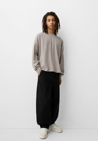 Light gray long-sleeve shirt with a relaxed fit, paired with loose black jeans and white sneakers. Simple design, soft texture.