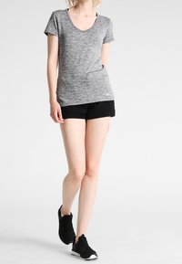 Grå melerad t-shirt med v-ringning och korta ärmar, kombinerad med svarta shorts och svarta sportskor. Enkel och figurnära design.