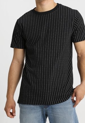 Czarna koszulka z pionowymi białymi paskami, krótki rękaw, okrągły dekolt i miękka, teksturowana tkanina. W komplecie z jasnoniebieskimi dżinsami.