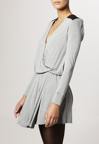 Robe grise à manches longues avec un décolleté en V, taille froncée et accents noirs contrastants sur les épaules. Fabriquée en tissu léger et doux.