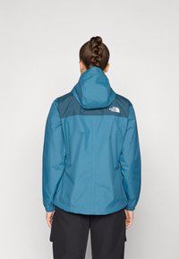 Blue waterproof jacket with a hood, featuring a dark blue shoulder panel, elastic cuffs, and The North Face logo on the back.
