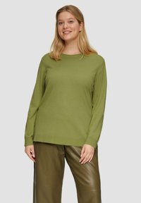 Groen gebreid pullover met een ronde hals en lange mouwen, gecombineerd met bruine leren broek. Soepele textuur en een relaxte pasvorm.