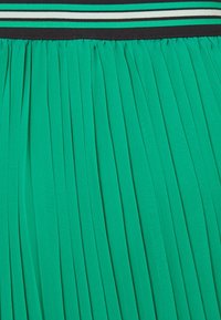 Gonna plissettata verde con un tessuto strutturato. Presenta una vita nera con strisce verdi e bianche alternate.