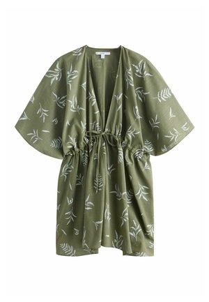Gros plan d'une robe verte avec des motifs de feuilles blanches, présentant une taille froncée nouée avec un nœud en tissu sur un vêtement intérieur noir.