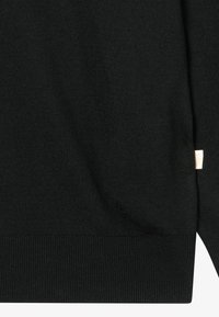 Μαύρος πλεκτός ύφασμα με  ribbed τελείωμα και μικρή λευκή ετικέτα με πορτοκαλί κείμενο στο πλάι του ρούχου.