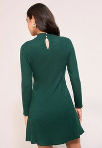 Roheline soonikute seeliku pikkade varrukatega kleit, millel on võtmeaugu seljapoolne detail, kaela juures kolm nupud ja laienev hemline.