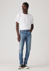 Tricou alb din bumbac, asortat cu blugi din denim bleu deschis. Blugii au o croială dreaptă și sunt purtați cu adidași alb-negru.
